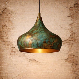 May include: A pendant light fixture with a green and gold finish. The light has a teardrop shape with a brass-colored top and a gold interior. The fixture hangs from a black cord.