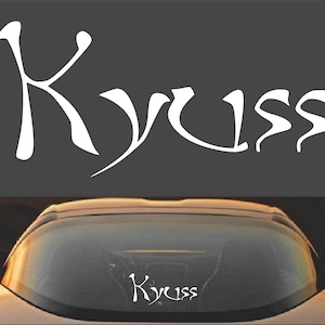 Puede incluir: Calcomanía de vinilo blanco con la palabra "Kyuss" escrita en una fuente estilizada. La calcomanía se muestra en la ventana trasera de un automóvil.