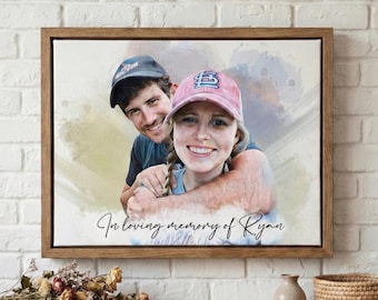 May include: A framed canvas print featuring a couple, with the text "In loving memory of Ryan." The artwork has a watercolor effect, with the couple wearing baseball caps. The frame is made of wood.