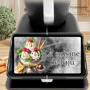 May include: A black kitchen appliance with a digital display featuring an ice cream dessert graphic. The display reads "La cuisine de Juju". The image also includes text that says "Personnalise ton look" and "Hand made with love".