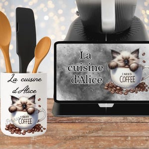Peut inclure: Un pot à ustensiles en céramique blanche avec le texte "La cuisine d'Alice" et un dessin de chat dans une tasse à café avec l'inscription "I NEED COFFEE". Le pot contient des cuillères en bois et une spatule noire. Un écran numérique affiche la même image.