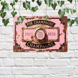 May include: A rectangular pink metal sign with the words "FOR CHAMPAGNE" and "CHAMPAGNE" in black. The sign has a gold-colored center with the words "PRESS PRESS RESS". The sign has a distressed, rusty appearance.