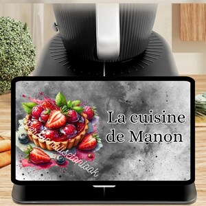 May include: A black kitchen appliance with a digital display showing a colorful image of a fruit tart with strawberries and blueberries. The text "La cuisine de Manon" is displayed on the screen.