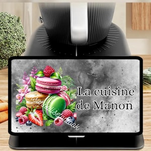 May include: A black digital display featuring a colorful illustration of macarons, berries, and flowers. The text "La cuisine de Manon" is displayed on the screen. The display is part of a black kitchen appliance.