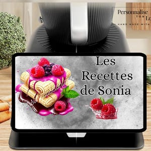 May include: A black kitchen appliance with a digital display showing the text "Les Recettes de Sonia". The display features an illustration of waffles with raspberries and blackberries, drizzled with pink sauce. The words "Personnalise ton Look" are also visible.