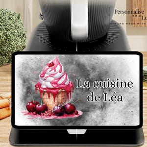 May include: A black digital kitchen scale with a screen displaying a colorful ice cream cone illustration with cherries and the text "La cuisine de Léa". The image also includes the text "Personnalise ton look".