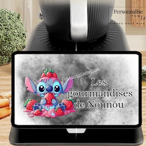 May include: A black tablet shows a cartoon character with strawberries and the text "Les gourmandises de Nounou". The tablet is set on a black base, with a kitchen appliance in the background.