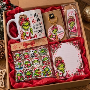 Peut inclure: Un coffret cadeau contenant une tasse en céramique blanche avec une illustration de personnage vert et du texte français, un porte-clés rond, un marque-page avec pompon, une planche de douze autocollants et un bloc-notes ligné, tous festifs.