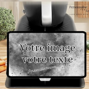 May include: A black tablet displays the text "Votre image votre texte" against a gray, speckled background. The tablet sits on a black base, with a black appliance in the background. The words "Personnalise ton look" are also visible.