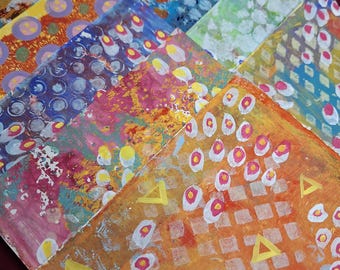May include: A collection of rectangular cards featuring abstract painted designs in vibrant colours including orange, yellow, pink, blue, and green. The surfaces display layered patterns of circles, grids, and triangles created with acrylic paint.