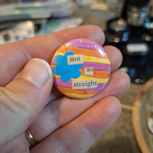 May include: A round button with the words "not so straight" on it. The button has a colorful background with orange, yellow, purple, and blue accents. The text is in a simple, easy-to-read font.
