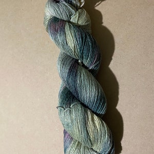 May include: A skein of yarn in shades of green, blue, and purple. The yarn is twisted into a spiral shape.