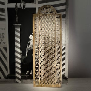 May include: A brass decorative door vent with a geometric pattern and a Greek key border. The vent is rectangular and has a slightly arched top.