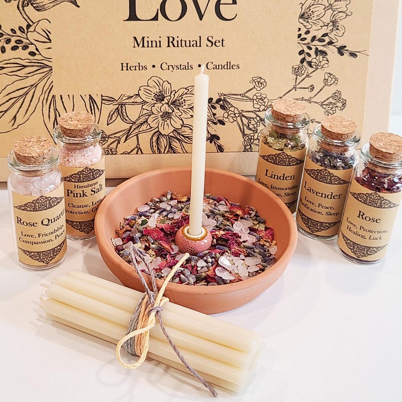 May include: A mini ritual set for love with a white candle, a small terracotta bowl filled with dried herbs and crystals, and four small glass bottles with labels that read "Rose Quartz", "Himalayan Pink Salt", "Linden", "Lavender", and "Rose".