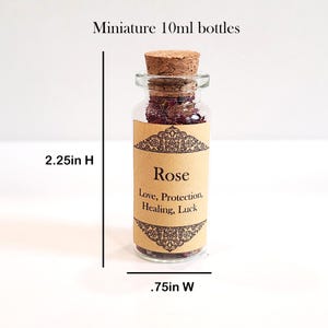 May include: A small glass bottle with a cork stopper filled with dried rose petals. The bottle has a label that reads "Rose" and "Love, Protection, Healing, Luck". The bottle is 2.25 inches tall and .75 inches wide.