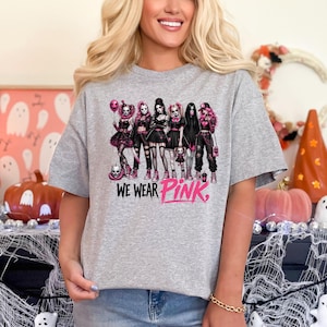 A woman wearing a gray t-shirt with a graphic design of a group of women in black and pink outfits, along with the text "WE WEAR PINK."