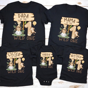 May include: Black t-shirts and a onesie with a jungle-themed design for a first birthday. Each shirt has a wooden sign with text like "Dada", "Mama", "Sister", "Brother", or a name, and "Wild One".