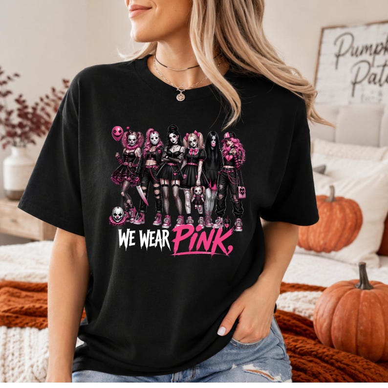 A woman wearing a black t-shirt with a graphic design featuring a group of women in various outfits, including a skull and crossbones, and the text "WE WEAR PINK" printed on the shirt.