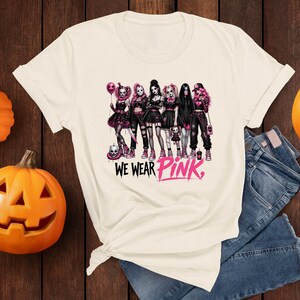A white t-shirt with a graphic design featuring a group of women dressed in dark clothing and accessories, along with the text "WE WEAR PINK."