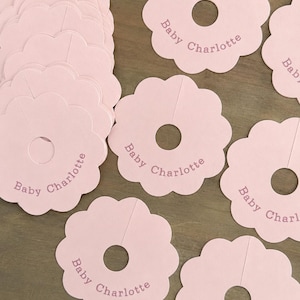 May include: A collection of light pink scalloped circular clothing dividers made of cardstock. Each divider features a central hole with a slit for hanging and is printed with the text Baby Charlotte in a simple, dark pink sans-serif font.
