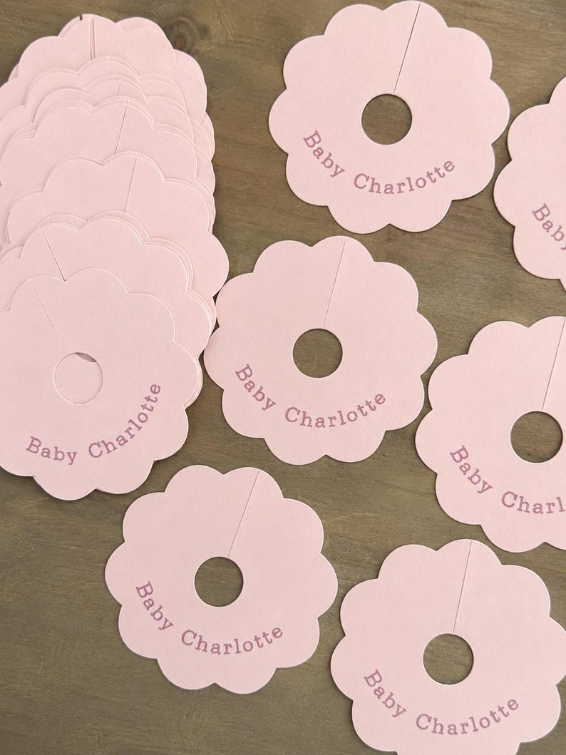 May include: A collection of light pink scalloped circular clothing dividers made of cardstock. Each divider features a central hole with a slit for hanging and is printed with the text Baby Charlotte in a simple, dark pink sans-serif font.
