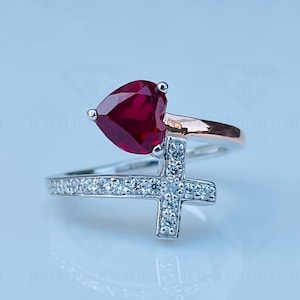 May include: A silver ring with a red heart-shaped stone and a cross design with clear stones.