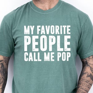 May include: A green t-shirt with white text that reads "My Favorite People Call Me Pop".