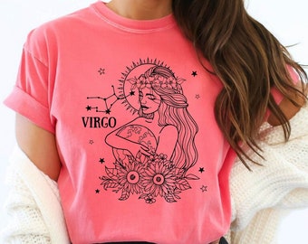 May include: A pink t-shirt with a black graphic design of a woman with a flower crown holding a globe. The graphic also includes the word "VIRGO" and stars.