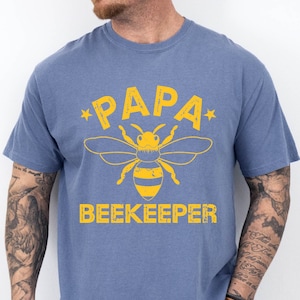 May include: A blue t-shirt with a yellow bee graphic and the text "*PAPA BEEKEEPER*" printed on the front.