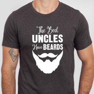 May include: A dark heather grey t-shirt with a white graphic that says "The Best Uncles Have Beards" and a white cartoon beard with a mustache.