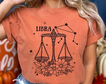 May include: A burnt orange t-shirt with a black Libra zodiac symbol and constellation design. The symbol is a set of scales with flowers underneath. The text "LIBRA" is above the scales.