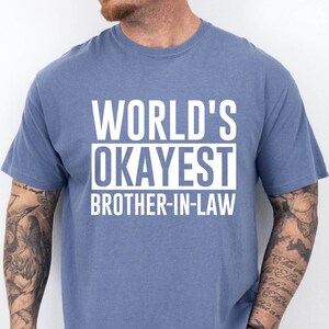 May include: A blue t-shirt with white text that reads "World's Okayest Brother-in-Law".