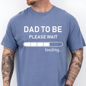 Puede incluir: Una camiseta azul con el texto "Dad to be Please Wait" y una barra de progreso que dice "loading..."