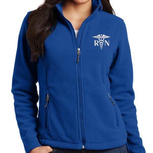 May include: A royal blue fleece jacket with a zipper closure and two pockets. The jacket has a white embroidered design of a medical caduceus with the letters "RN" below it.