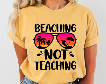 May include: A yellow t-shirt with the text "Beaching Not Teaching" and a graphic of sunglasses with palm trees and beach chairs reflected in the lenses.