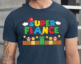 May include: A navy blue t-shirt with a graphic of a video game character and the text "SUPER FIANCE" in colorful letters. The graphic also includes a brick block, a question mark block, and a pipe.