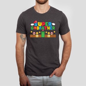 Puede incluir: Una camiseta gris oscuro jaspeada con un gr&aacute;fico de un personaje de Super Mario y el texto "SUPER GODFATHER".