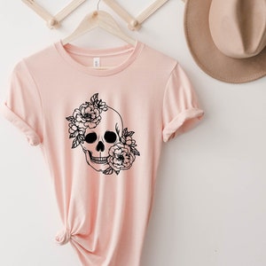 K&ouml;nnte beinhalten: Ein pinkfarbenes T-Shirt mit einem schwarz-wei&szlig;en Motiv eines Sch&auml;dels mit Blumen.
