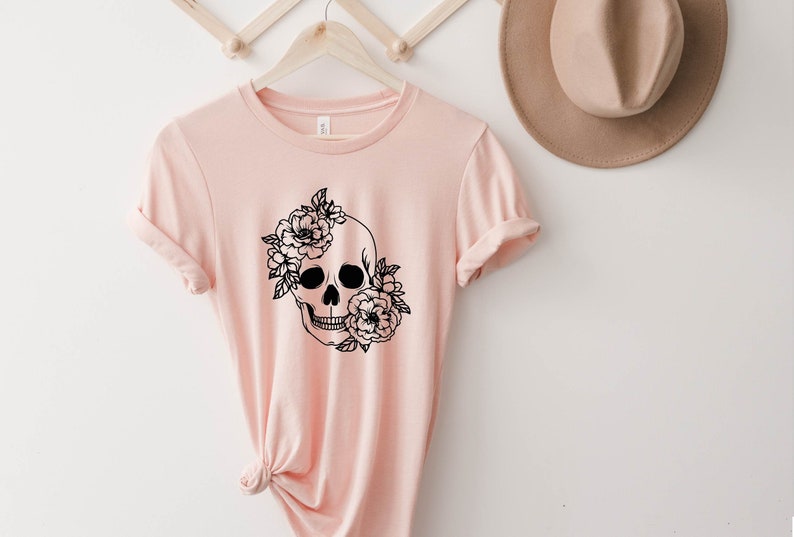 K&ouml;nnte beinhalten: Ein pinkfarbenes T-Shirt mit einem schwarz-wei&szlig;en Motiv eines Sch&auml;dels mit Blumen.