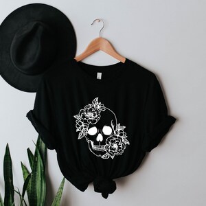 K&ouml;nnte beinhalten: Schwarzes T-Shirt mit einem wei&szlig;en floralen Totenkopf-Design.