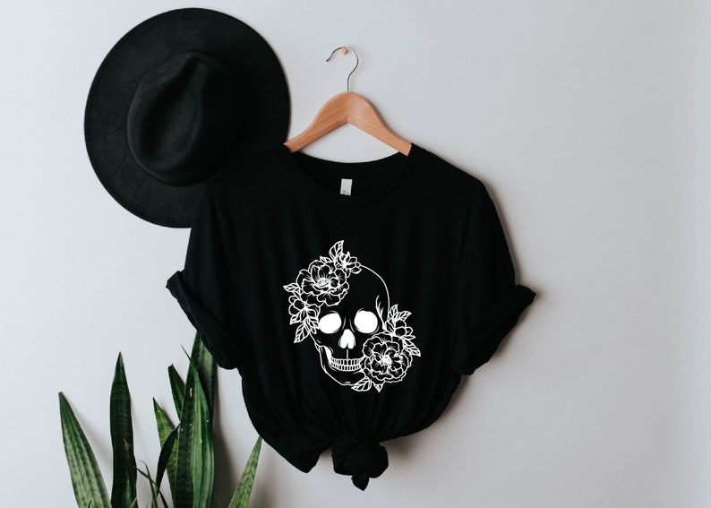 K&ouml;nnte beinhalten: Schwarzes T-Shirt mit einem wei&szlig;en floralen Totenkopf-Design.