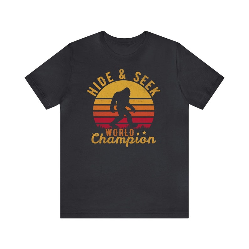 May include: Black t-shirt with a retro-style graphic of a Bigfoot walking in front of a sunset. The graphic says "Hide & Seek World Champion".
