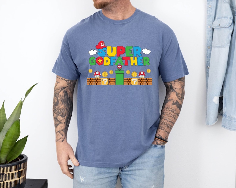 Puede incluir: Una camiseta azul con un gr&aacute;fico de un personaje de Super Mario Bros. y el texto "SUPER GODFATHER".