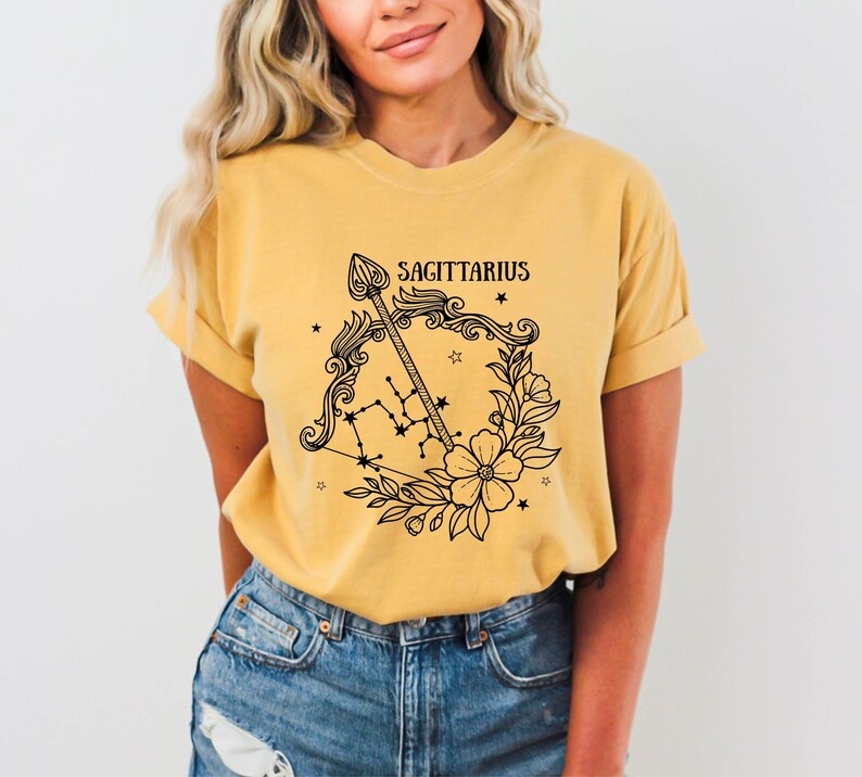 May include: A yellow t-shirt with a black graphic of the Sagittarius zodiac sign, featuring an arrow, bow, and floral design. The text "SAGITTARIUS" is printed above the graphic.