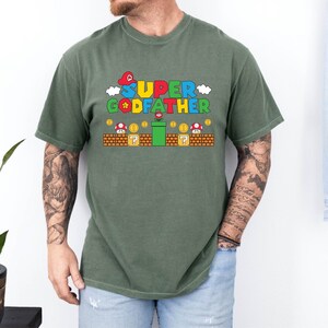 Puede incluir: Una camiseta verde con un gr&aacute;fico de un personaje de videojuego y el texto "SUPER GODFATHER".