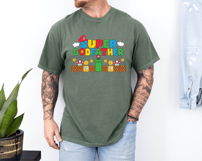 Puede incluir: Una camiseta verde con un gr&aacute;fico de un personaje de videojuego y el texto "SUPER GODFATHER".