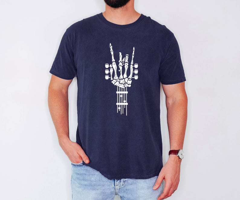 Pu&ograve; includere: Una t-shirt blu navy con una grafica bianca di una mano scheletrica che suona la chitarra. La mano sta facendo il gesto rock and roll.