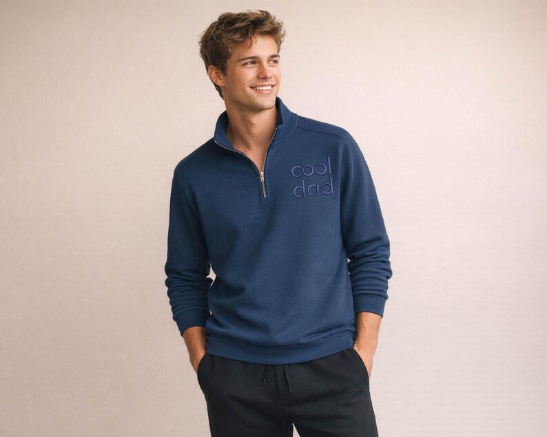 May include: A navy blue pullover sweatshirt with a quarter-zip collar and the embroidered text "cool dad". The long-sleeved top is made of a soft material and has a relaxed fit. The model is wearing black pants.