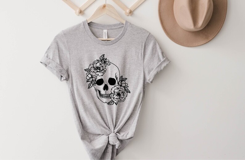 K&ouml;nnte beinhalten: Ein graues T-Shirt mit einer schwarz-wei&szlig;en Illustration eines Sch&auml;dels mit Blumen.