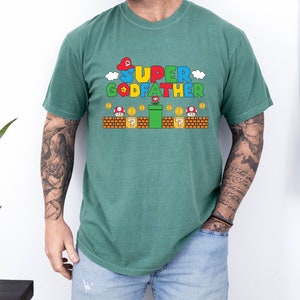 Puede incluir: Una camiseta verde con un gr&aacute;fico de un personaje de Super Mario Bros. sosteniendo una flor y el texto "SUPER GODFATHER".
